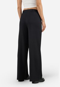 Black wide-leg pants with a smooth fabric, featuring a standard waistband, rear pockets, and a straight fit from the waist to the floor.
