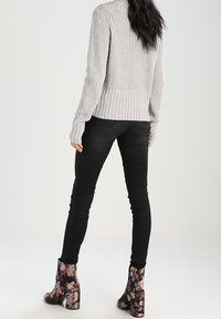 Maglione grigio a coste abbinato a jeans skinny neri e stivaletti con motivo floreale e tacco grosso.