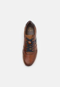Barna bőrből készült sneaker perforált textúrával, sötétkék fűzőkkel és barna nyelvvel. Oldalán logó látható, és párnázott talpbetéttel rendelkezik.