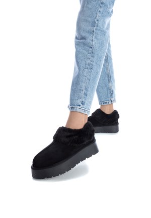 Zapatos de plataforma negros hechos de gamuza con ribete de piel sintética. Presentan una puntera redondeada y suela de goma texturizada. Combinados con unos jeans de color azul claro.