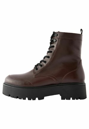 Bottine en cuir marron avec des lacets noirs, bout rond et semelle épaisse et texturée. Présente des coutures contrastées et des accents latéraux subtils.