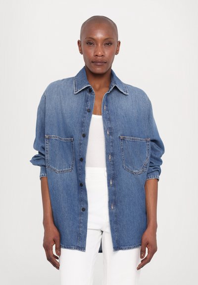 Denim shirt with a button-up design, features a classic collar, two front pockets, and rolled sleeves. Light blue color with a slight fade.