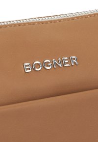 Borsa in tessuto beige con logo "BOGNER" in tono argento, chiusura con zip e dettagli metallici, texture liscia e sottili accenti di cucitura.