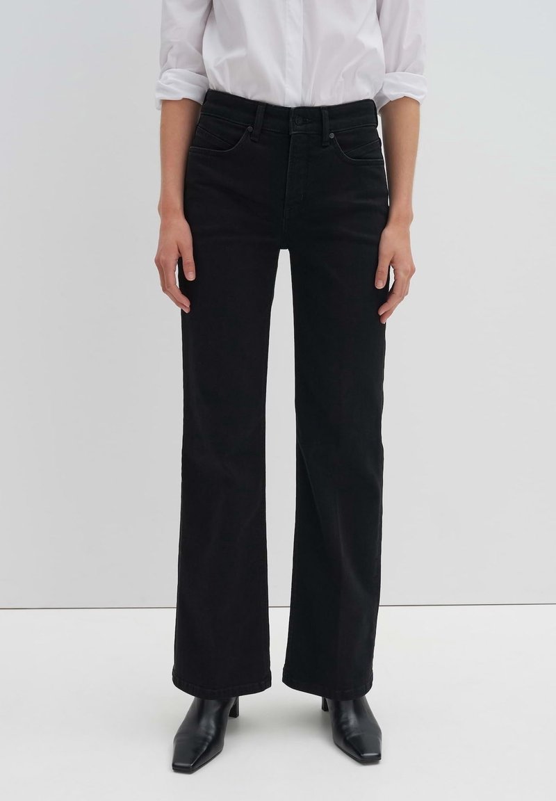 Black wide-leg jeans with five pockets, made from denim fabric. Features a high waist and classic stitching. Worn with pointed black heels.