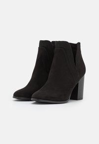 Svarta mocka ankle boots med spetsiga tår och staplade klackar. Har en scalloped-design vid kragen och en texturerad sula.