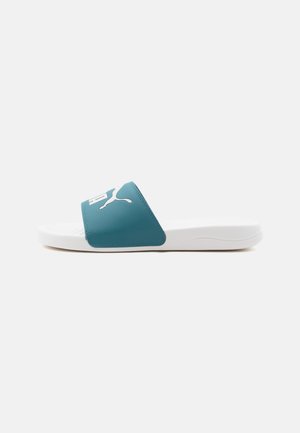 White slide sandal with blue strap featuring white Puma logo, flat sole, and textured footbed on plain background.