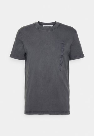 T-shirt a maniche corte di colore grigio scuro con scollo rotondo e ricamo verticale "Calvin Klein Jeans" sul lato sinistro del petto.