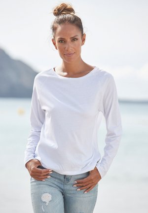 White long-sleeve shirt made of a lightweight fabric, featuring a scoop neckline and relaxed fit, paired with light blue distressed jeans.