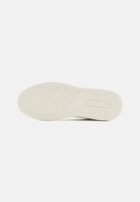 White rubber shoe sole with wave pattern and raised branding detail. Smooth texture and rounded shape. Designed for optimal grip and support.