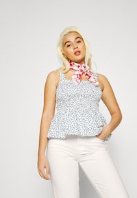 Top peplum floral azul e branco com detalhes de frunces e alças finas; combinado com um lenço com padrão de cerejas vermelhas e brancas.