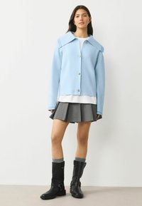 Jasnoniebieska krótka kurtka z dużym kołnierzem, srebrnymi guzikami, noszona na białej koszuli, zestawiona z plisowaną szarą spódnicą i czarnymi kozaczkami za kolano.