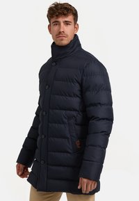 Marinepufferjack met een hoge kraag, knopenfront en een quilted ontwerp. Voorzien van een zijzak met een leren logo-accent. Zachte stoftextuur.