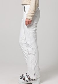 Witte skibroek van waterafstotend materiaal, voorzien van ritszakken en een aansluitend ontwerp. Aan de onderkant van het been bevindt zich een logo aan de zijkant.