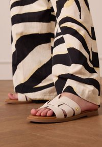 White leather sandals with cut-out design and tan sole, paired with black and white striped wide-leg pants featuring yellow accents.