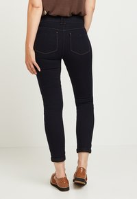 Slanka mörkblå jeans med uppvikta fållar, med bakfickor och kontrasterande sömmar. Tyget har en slät yta.