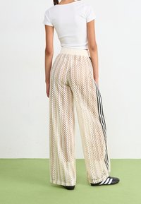 Kermavaaleat leveät housut, joissa on verkkomuotoinen kuvio, mustat viivakoristeet sivuilla ja korkea joustava vyötärö.