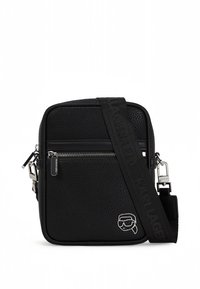 Svart teksturert skulderveske med glidelåslomme foran, bred justerbar stropp med preget merkenavn, og lite sølvfarget logoemblem.