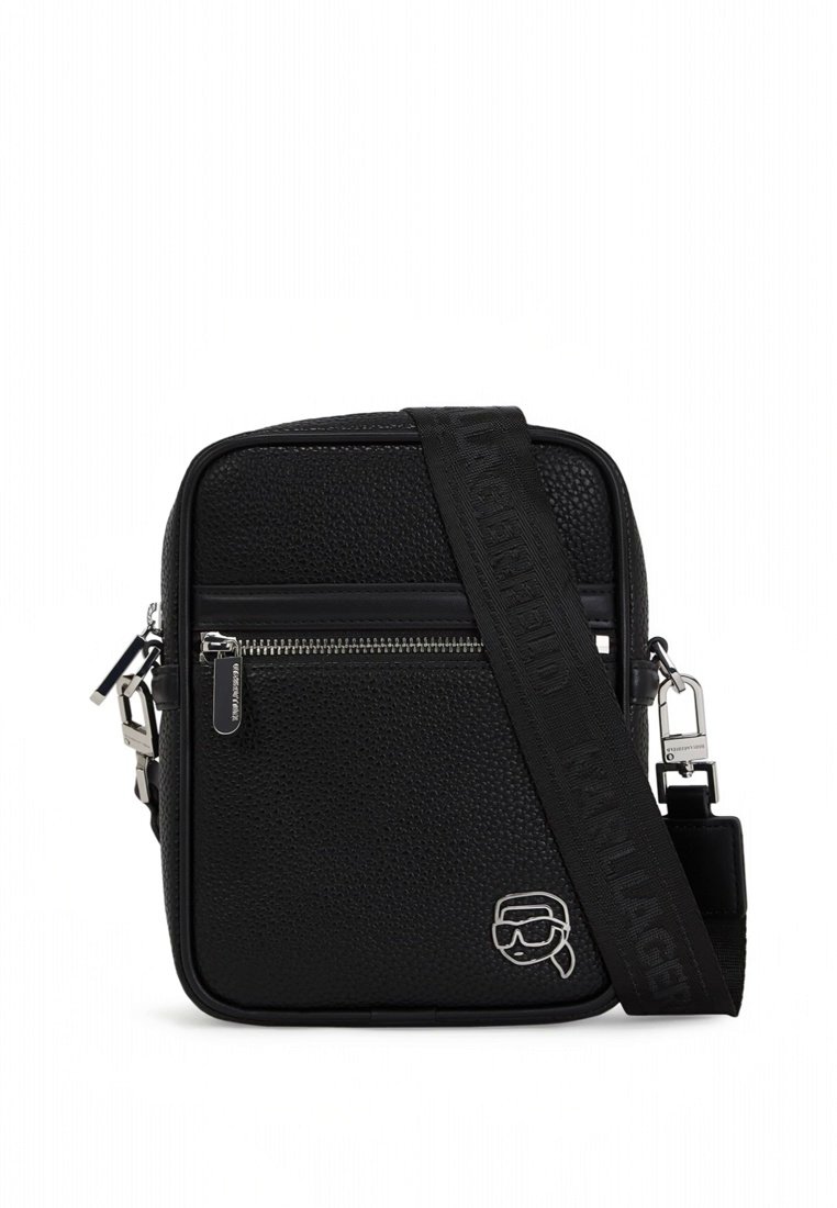 Sac bandoulière noir texturé avec poche zippée à l'avant, large sangle réglable avec nom de la marque embossé, et petit emblème logo argenté.