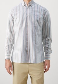 Camicia a righe bianche con linee blu e rosse, con colletto, maniche lunghe e un piccolo logo sul petto.