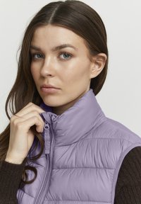Lila puffy vest met een hoge kraag en ritsluiting; heeft een horizontaal gestikt patroon en lichtgewicht, glanzend materiaal.