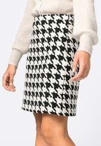 Neulehame, jossa on mustavalkoinen hounds-tooth-kuvio, suora leikkaus ja teksturoitu kangas. Käsi lepää sivulla.