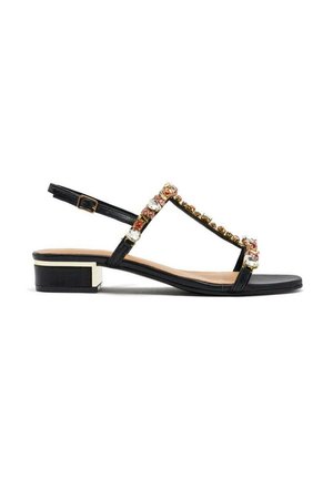 Sandale en cuir noir avec un design à lanière en T, ornée d'accents en or et en cristal, et d'un petit talon bloc, dotée d'une sangle de cheville à boucle.