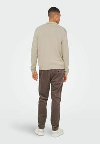 Beige strikket sweater med ribbede manchetter og kant, parret med brune fløjlshoser. Hvide sneakers fuldender outfittet.