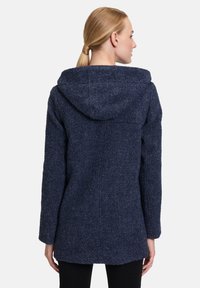 Granatowy, strukturalny płaszcz z kapturem, o prostym kroju i długich rękawach. Materiał wydaje się ciepły i odpowiedni na chłodniejsze temperatury.