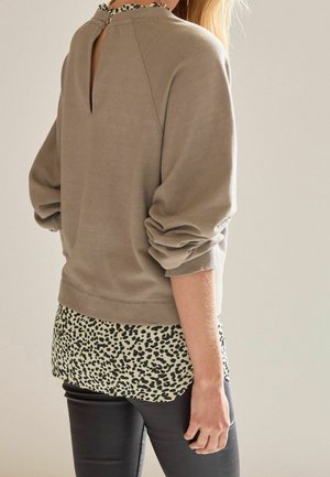 Beige sweatshirt met ballonmouwen, voorzien van een sleutelgatdetail op de rug en een leopardenprintboord. Gecombineerd met zwarte skinny pants.