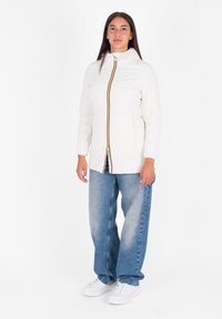 Witte lichtgewicht jas met een ritssluiting voor en kleurrijke verticale streepdetaillering. Draagt over blauwe, losse jeans en witte sneakers.