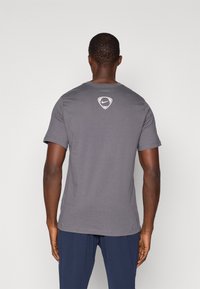 Maglietta grigia a maniche corte realizzata in cotone, con scollatura rotonda e un logo Nike bianco discreto sulla parte superiore della schiena.
