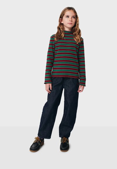 Langärmliges, geripptes Oberteil mit grünen und roten horizontalen Streifen, kombiniert mit marineblauen gestreiften weit geschnittenen Hosen und schwarzen Schnürschuhen.