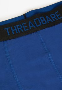 Primer plano de unos bóxers azules con cinturilla elástica negra que muestra el nombre de la marca "THREADBARE" en letras azules.