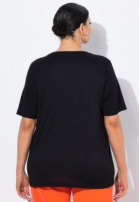 Schwarzes T-Shirt mit kurzen Ärmeln, lockere Passform, weicher Stoff. Auffälliger Rundhalsausschnitt und glatte Textur. Tragen mit leuchtend orangefarbenen Hosen.