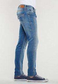 Skinny fit blauwe denim jeans met een vervaagde afwerking, voorzien van achterzakken, een bruine leren patch op de taille en subtiele stikdetails.