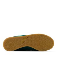 Zapatilla de ante verde con suela de goma de color natural que presenta un patrón de suela circular y un logotipo en relieve. Diseño minimalista y estructura flexible.