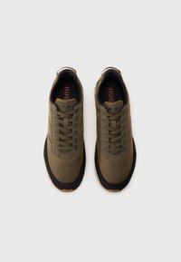 Olive green athletic shoes with a textured upper, round toe, and black rubber sole. Features lace closure and logo detail on the tongue.