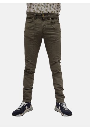 Pantaloni elasticizzati khaki con una vestibilità slim, dotati di tasche laterali e chiusura con bottone. Indossati con sneakers blu navy e una camicia a fantasia.