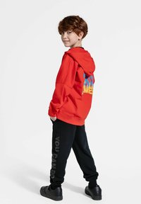 Czerwona bluza z kapturem z kolorowym napisem z tyłu, zestawiona z czarnymi spodniami dresowymi z grafiką "MOŻESZ ZROBIĆ". Czarne trampki dopełniają strój.