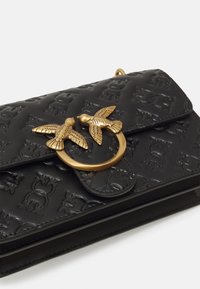 Zwarte geperforeerde lederen handtas met een goudkleurige vogelmotief sluiting en een slank ontwerp met een gestructureerd oppervlak.