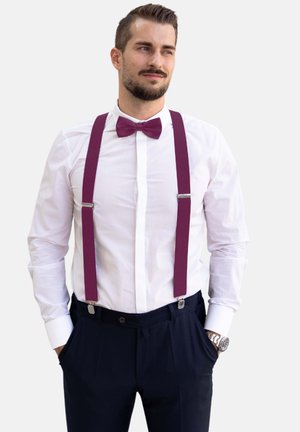 Chemise blanche à manches longues, associée à un pantalon navy foncé et des bretelles couleur prune. Le nœud papillon coordonné aux bretelles. Quincaillerie en argent visible.