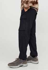 Svarta cargo byxor med avslappnad passform, med en sidficka, tillverkade av ett slätt tyg, som är kombinerade med grå sneakers. En strukturerad fleece-tröja syns.