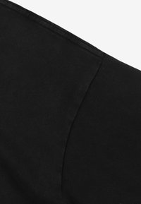 Czarna tkanina o gładkiej strukturze i matowym wykończeniu, z zaokrągloną detalem szwu na krawędzi. Brak widocznych wzorów lub metalowych elementów.