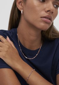 Smykkesæt i rosaguldbelagte materialer inklusive en tynd kæde, et matchende armbånd og øreringe med et elegant design og glat tekstur.