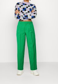 Person wearing green high-waist trousers, white chunky sneakers, and a cropped checkered sweater in lavender, blue, black, and mint colors.