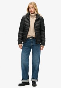 Czarna kurtka puchowa z wysokim kołnierzem, beżowy sweter z golfem, luźne dżinsy oraz czarne botki. Wyróżnia się pikowaną fakturą i swobodnym krojem.