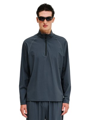 Mann trägt dunkelgraues Langarm-Halbzip-Shirt und passende Hose, mit schwarzen Wraparound-Sonnenbrillen, steht vor weißem Hintergrund.