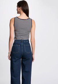 Stribet ærmeløs top i sort og hvid, parret med højtaljede mørkeblå denimbukser med lige ben og to baglommer.