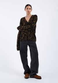 Czarny i złoty kardigan w wzory dzianinowe z dekoltem w serek i guzikami, zestawiony z oversize'owymi granatowymi dżinsami i brązowymi loafersami.
