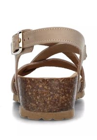 Sandalo beige con cinturini e tacco basso in sughero, dettagliato con una fibbia argentata. I cinturini creano un motivo incrociato per un supporto aggiuntivo.
